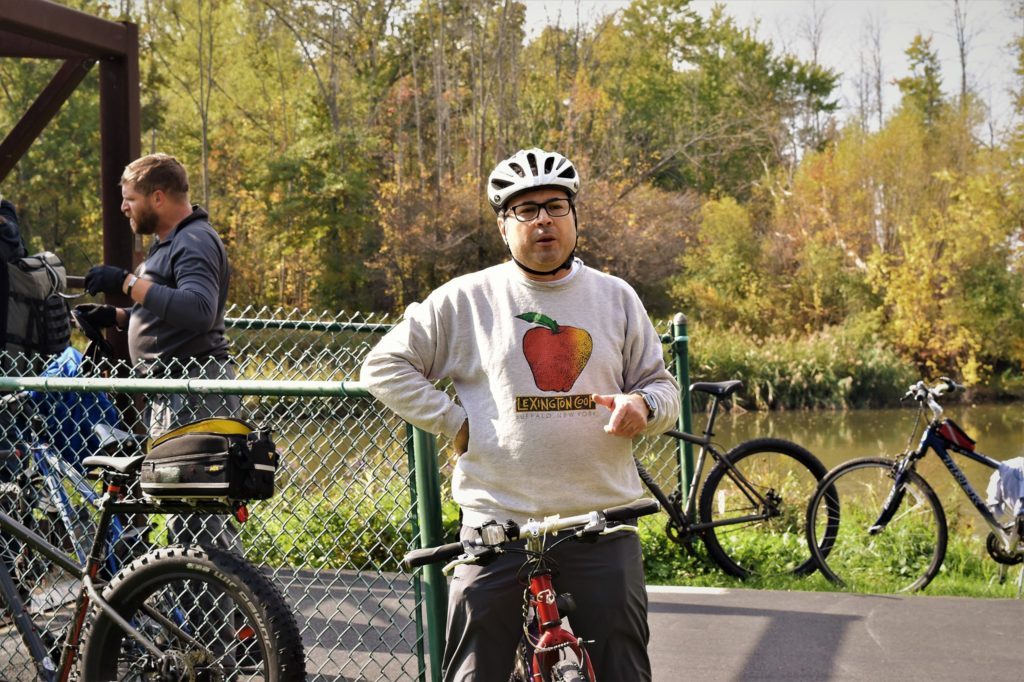 Dom Licata, wearing a bike helmet and sitting on his bike, speaking to riders where the Peanut Line meets the Ellicott Trail path.