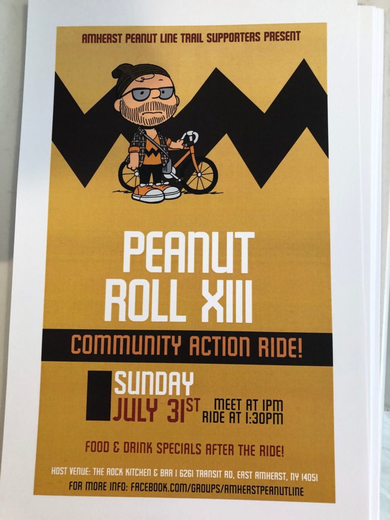 Poster: Peanut Roll mascot and bike. Text: Amherst Peanut Line Trail Supporters Present: Peanut Roll XIII Community Action Ride! Sunday, July 31st. Meet at 1pm. Ride at 1:30pm. Food and drink specials after the ride! Host venue: The Rock Kitchen and Bar, 6261 Transit Road, East Amherst, NY 14051. For more info: Facebook.com/groups/amherstpeanutline.